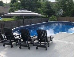 patio lounges and umbrella near swimming pool with concrete deck installation
