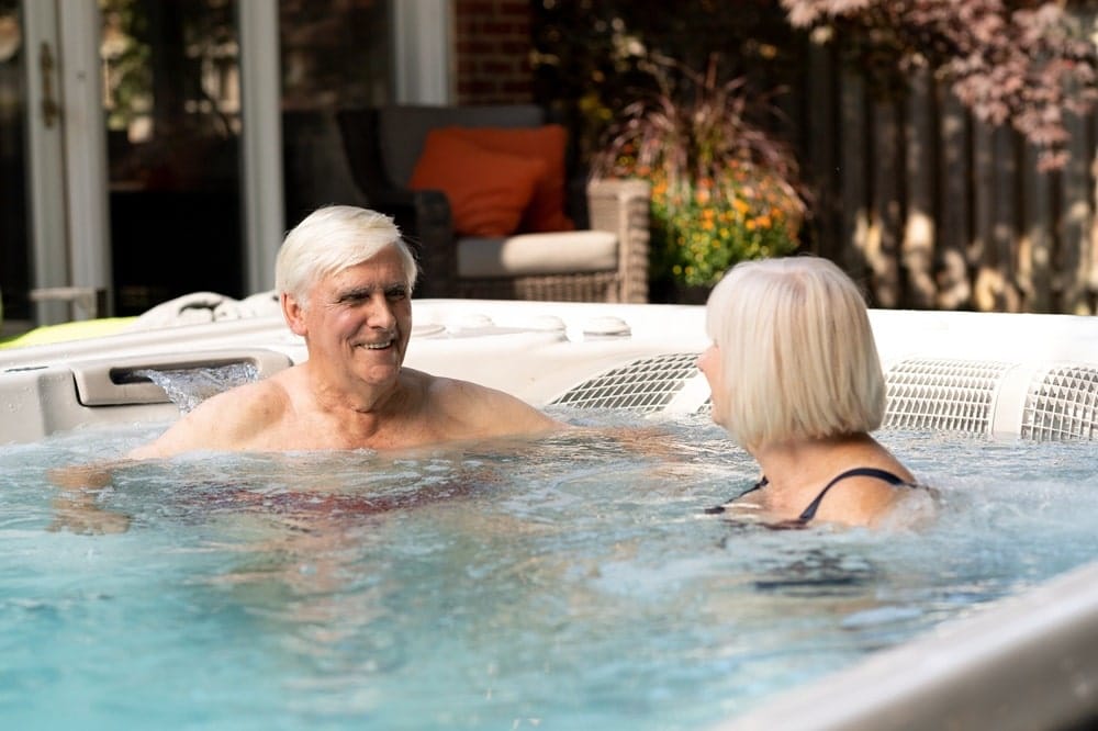 Two elderly people relaxing in a swim spa in a backyard setting
