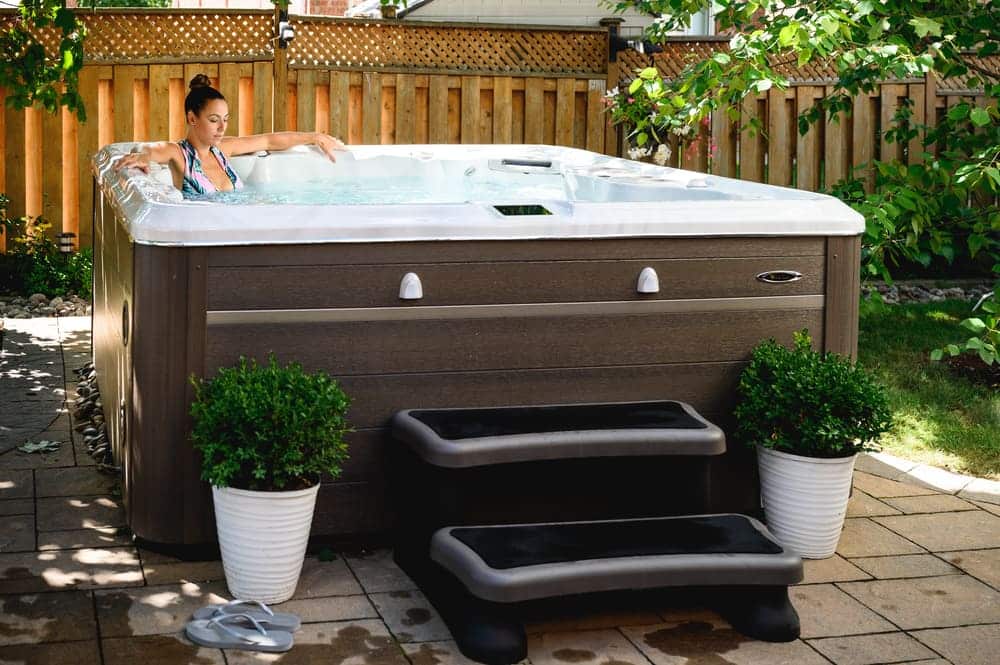 woman in a hot tub installed in a backyard surrounded with wooden fence