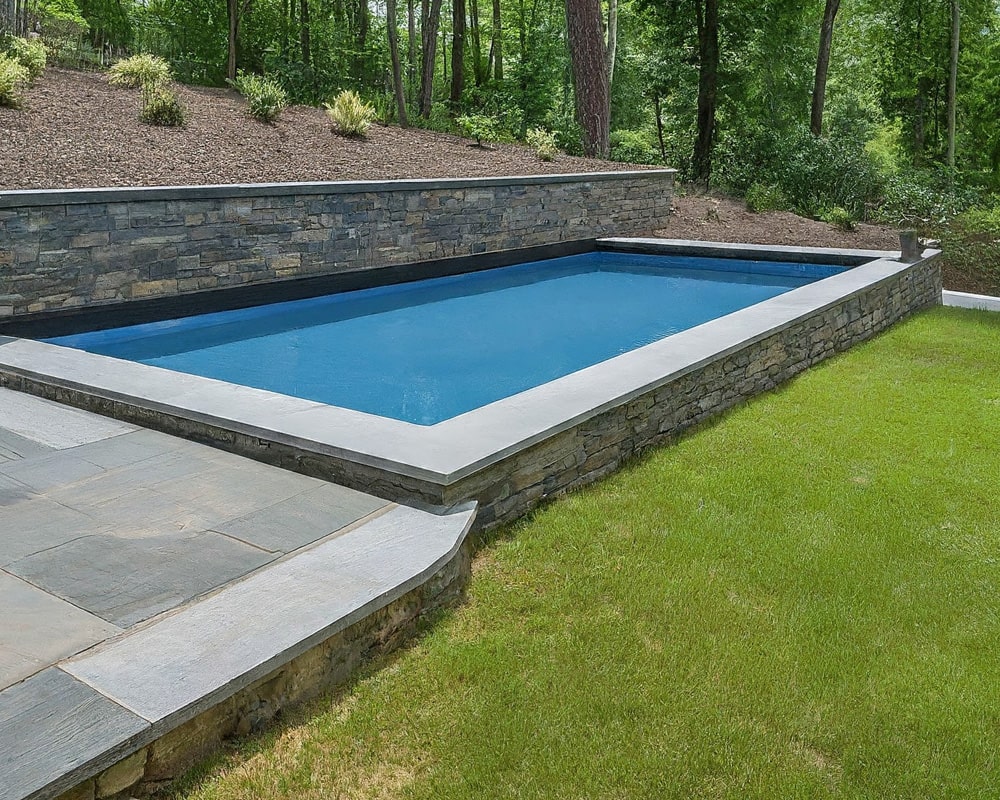 semi-inground pool with a blue liner and a light colored flagstone patio surrounding it