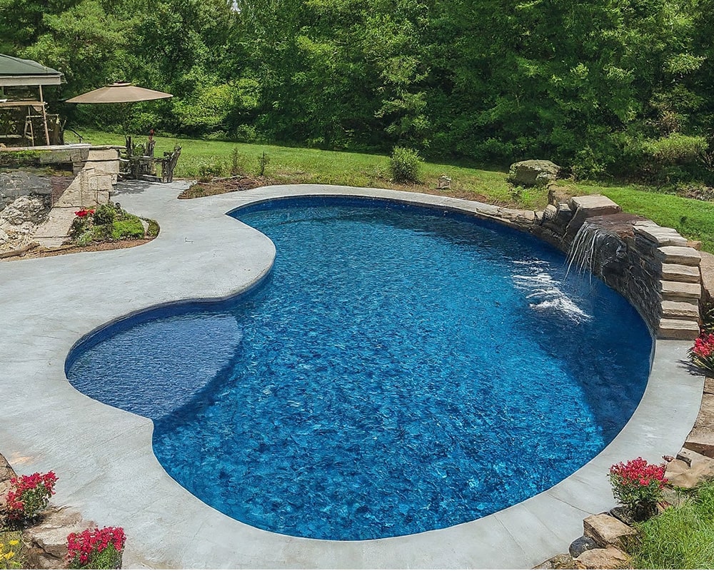 Luxurious kidney-shaped vinyl swimming pool with a waterfall feature, surrounded by a well-manicured garden and patio area